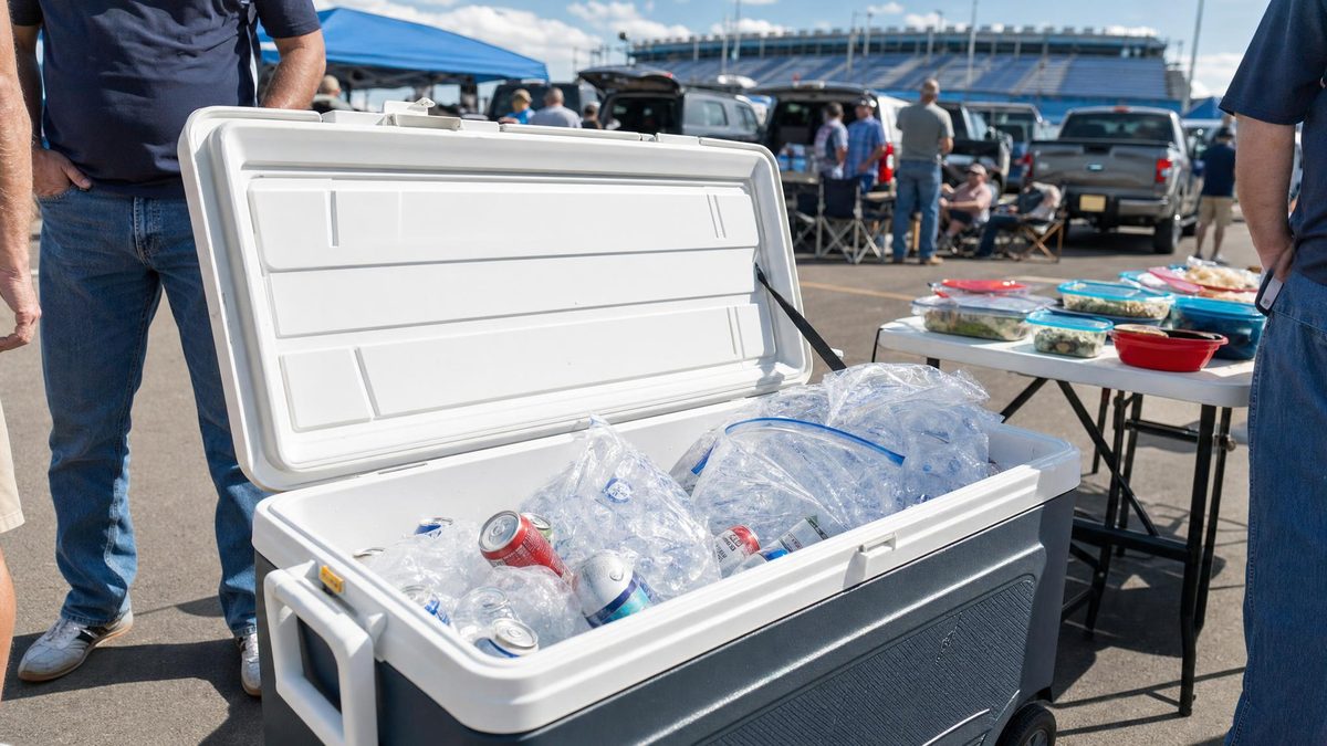 Cooler packed with bagged ice and drinks at an outdoor tailgate in a stadium parking lot